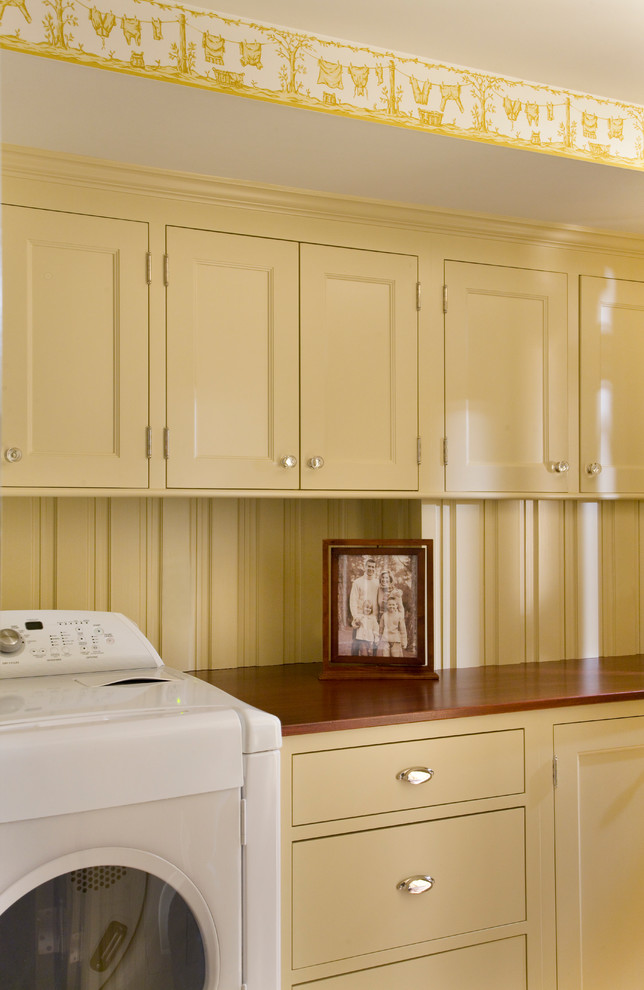 Imagen de cuarto de lavado lineal tradicional de tamaño medio con armarios con paneles empotrados, puertas de armario amarillas, encimera de madera, paredes amarillas y lavadora y secadora juntas