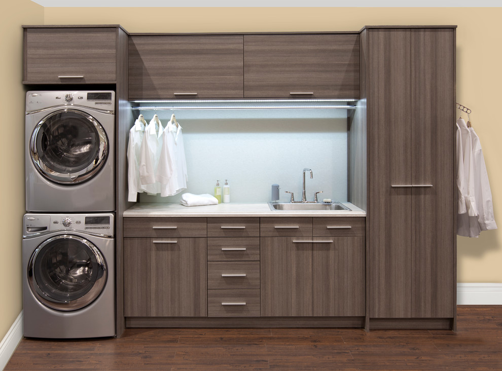 Photo of a medium sized contemporary single-wall utility room in Toronto with a built-in sink, flat-panel cabinets, beige walls, dark hardwood flooring, a stacked washer and dryer and grey cabinets.