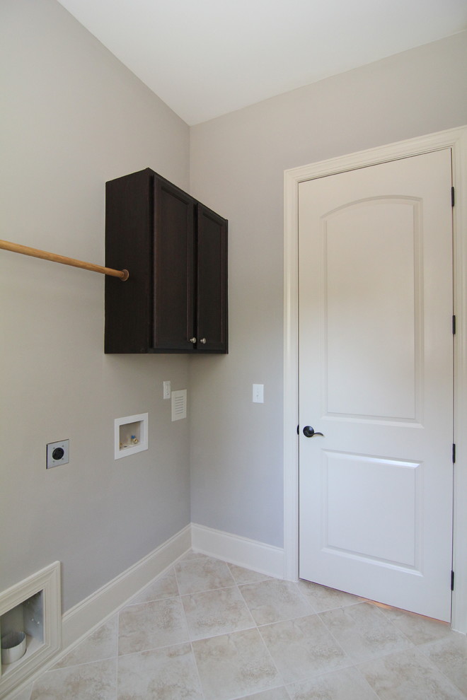 Example of a mid-sized classic l-shaped ceramic tile utility room design in Raleigh with a single-bowl sink, recessed-panel cabinets, dark wood cabinets, solid surface countertops, gray walls and a side-by-side washer/dryer