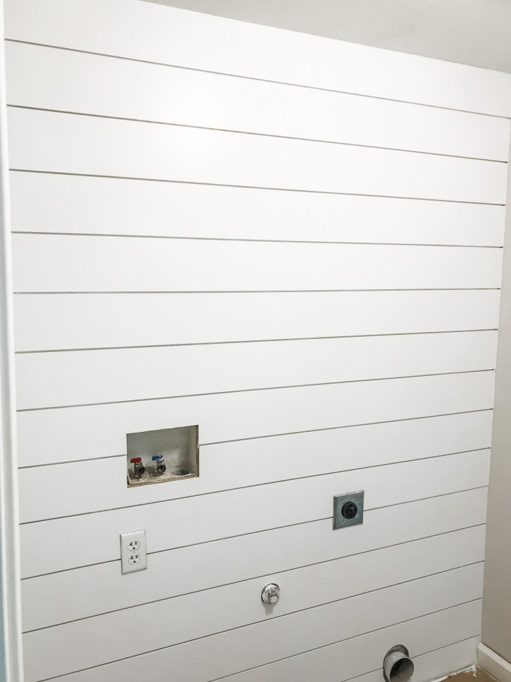 Bild på ett litet lantligt grå linjärt grått grovkök, med öppna hyllor, vita skåp, träbänkskiva, vita väggar, klinkergolv i porslin, en tvättmaskin och torktumlare bredvid varandra och beiget golv