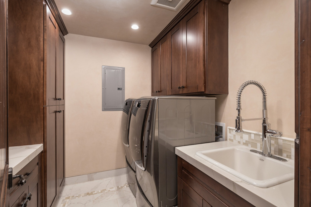 Mid-sized minimalist u-shaped ceramic tile and multicolored floor utility room photo in San Francisco with a farmhouse sink, shaker cabinets, brown cabinets, marble countertops, beige walls and a side-by-side washer/dryer