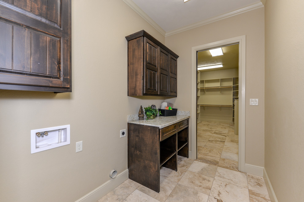 Photo of a medium sized rustic single-wall utility room in Other with raised-panel cabinets, dark wood cabinets, granite worktops, beige walls, travertine flooring, a side by side washer and dryer and multi-coloured floors.