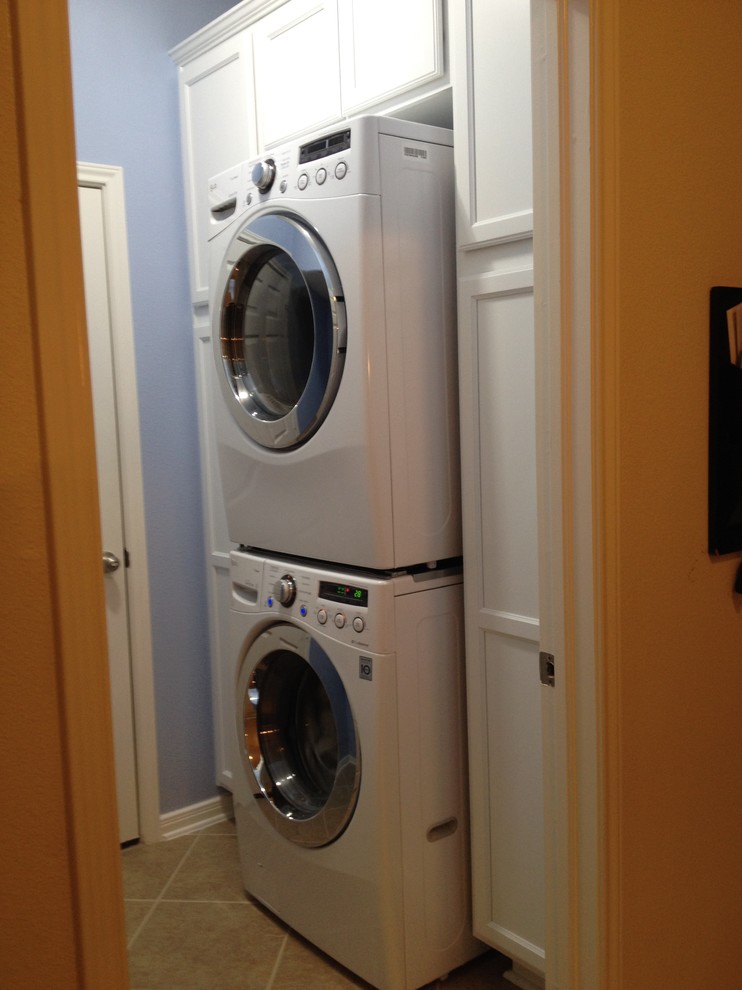 Immagine di una piccola sala lavanderia costiera con ante con riquadro incassato, ante bianche, pareti blu, pavimento con piastrelle in ceramica e lavatrice e asciugatrice a colonna