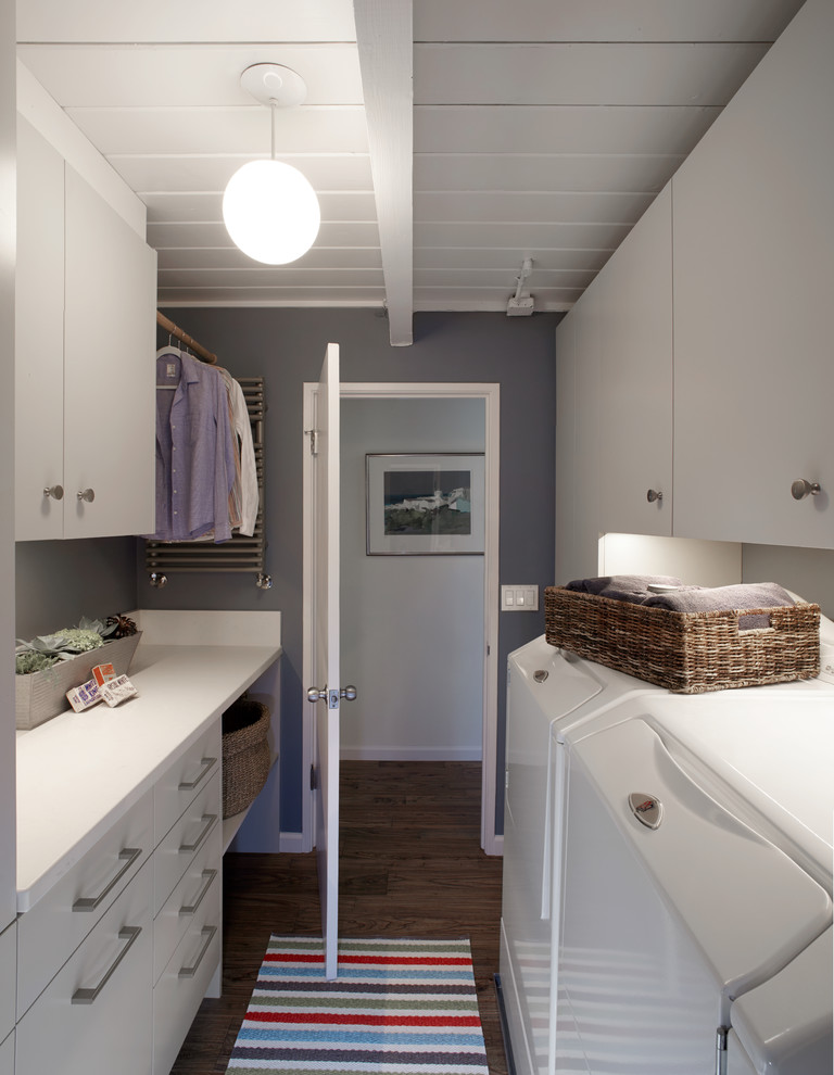 Bild på en liten funkis parallell tvättstuga enbart för tvätt, med släta luckor, marmorbänkskiva, grå väggar, en tvättmaskin och torktumlare bredvid varandra och vita skåp