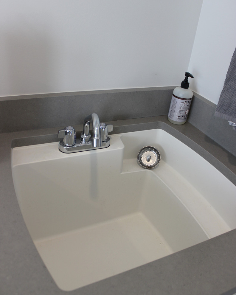 Inspiration för mellanstora klassiska linjära grått tvättstugor enbart för tvätt, med en undermonterad diskho, släta luckor, vita skåp, bänkskiva i kvarts, klinkergolv i keramik, en tvättmaskin och torktumlare bredvid varandra och grått golv