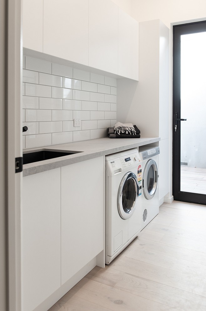 Idéer för att renovera en mellanstor funkis grå parallell grått tvättstuga enbart för tvätt, med en undermonterad diskho, öppna hyllor, vita skåp, bänkskiva i kvarts, vita väggar, ljust trägolv och en tvättmaskin och torktumlare bredvid varandra