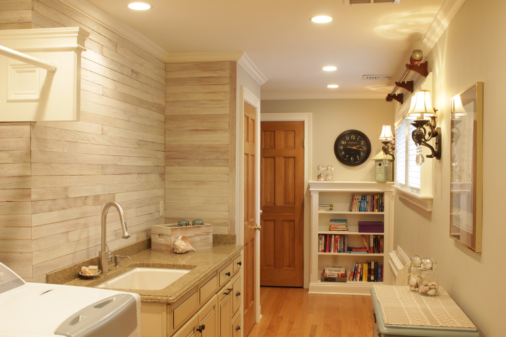 Photo of a large country single-wall utility room in New York with a submerged sink, raised-panel cabinets, beige cabinets, granite worktops, grey walls, medium hardwood flooring, a side by side washer and dryer, brown floors, grey splashback, wood splashback and tongue and groove walls.