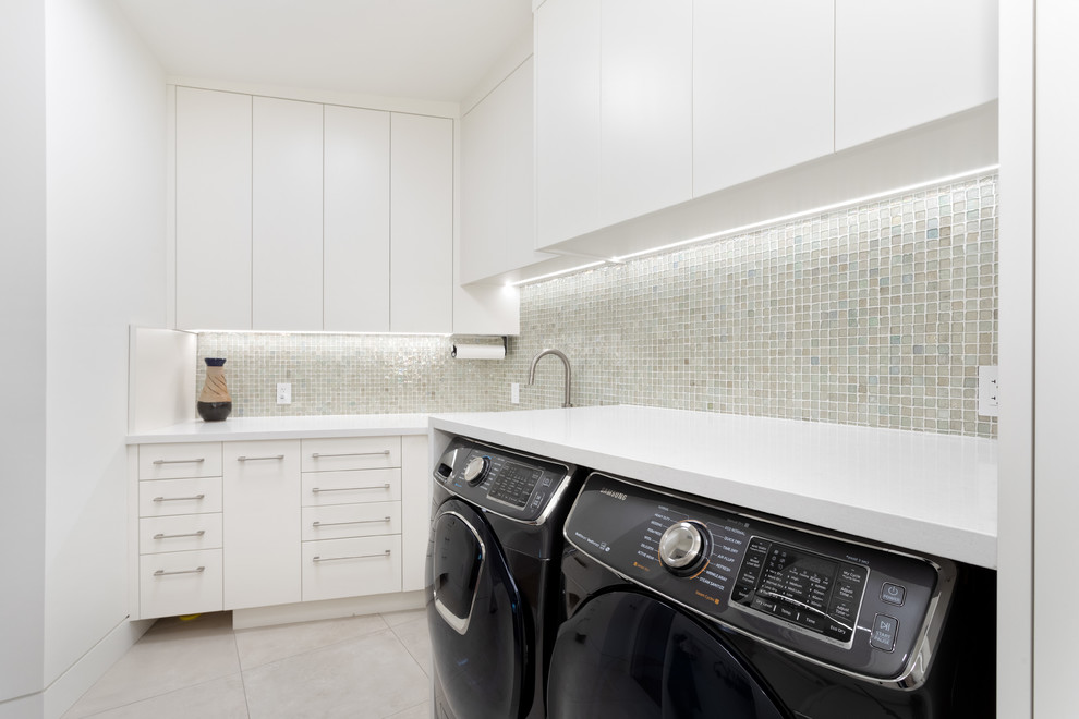 Inspiration för stora moderna l-formade vitt tvättstugor enbart för tvätt, med släta luckor, vita skåp, bänkskiva i kvartsit, klinkergolv i keramik, en tvättmaskin och torktumlare bredvid varandra, beiget golv och vita väggar