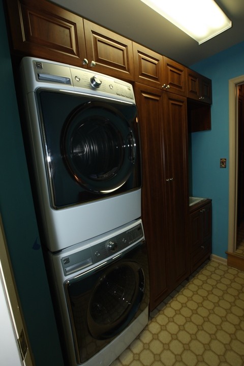 Immagine di una lavanderia multiuso chic di medie dimensioni con ante con bugna sagomata, ante in legno scuro, pareti blu e lavatrice e asciugatrice a colonna