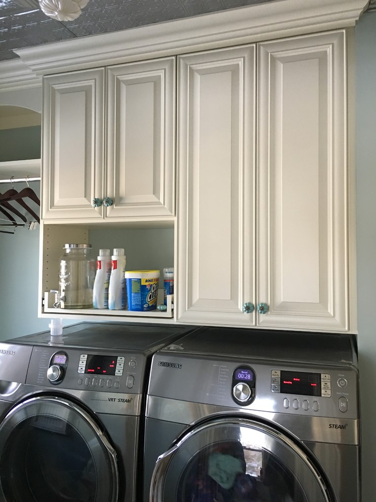 Design ideas for a medium sized classic l-shaped utility room in Minneapolis with a belfast sink, raised-panel cabinets, white cabinets, blue walls, ceramic flooring and a side by side washer and dryer.