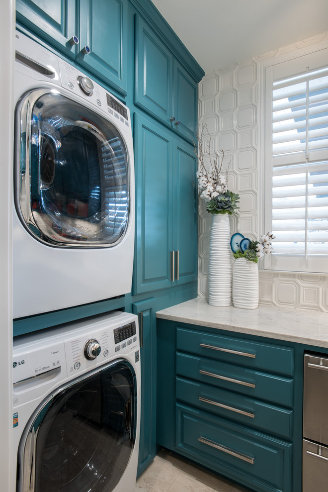 Modelo de cuarto de lavado tradicional con armarios con paneles con relieve, puertas de armario turquesas, paredes blancas, lavadora y secadora apiladas y encimeras blancas