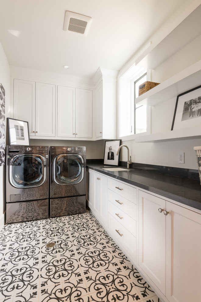 Foto di una sala lavanderia tradizionale con lavello sottopiano, ante con riquadro incassato, ante bianche, lavatrice e asciugatrice affiancate, pavimento multicolore e top nero