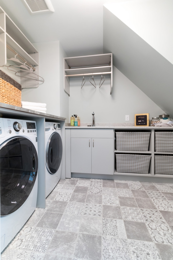 Bild på en mellanstor funkis l-formad tvättstuga enbart för tvätt, med en undermonterad diskho, släta luckor, grå skåp, laminatbänkskiva, grå väggar, klinkergolv i porslin och en tvättmaskin och torktumlare bredvid varandra