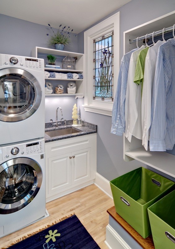 Idéer för små funkis l-formade tvättstugor enbart för tvätt, med en undermonterad diskho, luckor med upphöjd panel, vita skåp, granitbänkskiva, blå väggar, ljust trägolv och en tvättpelare