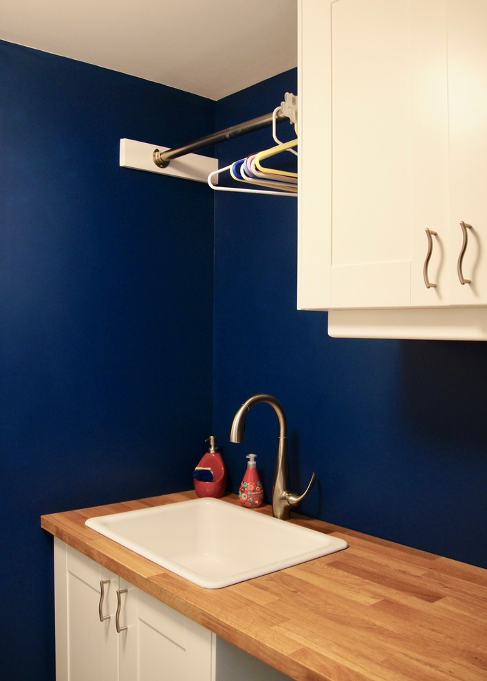 Inspiration för små moderna parallella brunt tvättstugor enbart för tvätt, med en enkel diskho, skåp i shakerstil, vita skåp, träbänkskiva, blå väggar, mellanmörkt trägolv, en tvättmaskin och torktumlare bredvid varandra och brunt golv