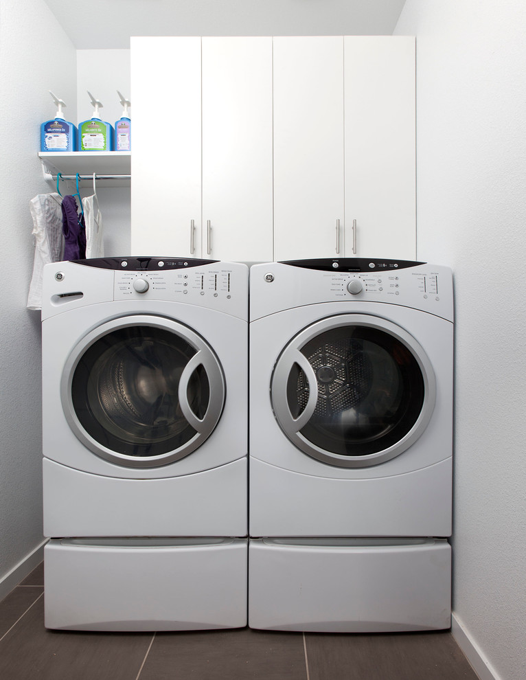 Inspiration for a small modern single-wall utility room in Toronto with flat-panel cabinets, white cabinets and a side by side washer and dryer.