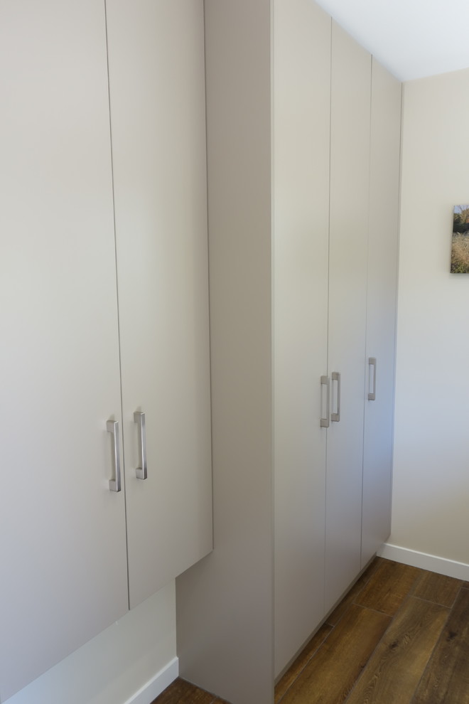 This is an example of a contemporary galley utility room in Auckland with a submerged sink, flat-panel cabinets, beige cabinets, laminate countertops, white walls, ceramic flooring and a side by side washer and dryer.