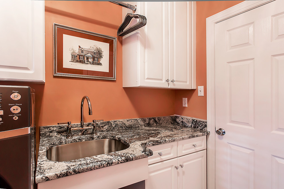 Bild på en liten vintage linjär tvättstuga enbart för tvätt, med en undermonterad diskho, skåp i shakerstil, vita skåp, granitbänkskiva, orange väggar, klinkergolv i porslin och en tvättmaskin och torktumlare bredvid varandra
