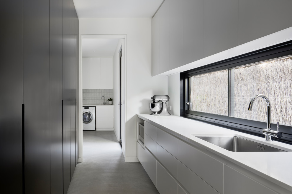 Zweizeilige, Mittelgroße Moderne Waschküche mit Unterbauwaschbecken, flächenbündigen Schrankfronten, weißen Schränken, Quarzwerkstein-Arbeitsplatte, weißer Wandfarbe, Betonboden, grauem Boden und weißer Arbeitsplatte in Melbourne