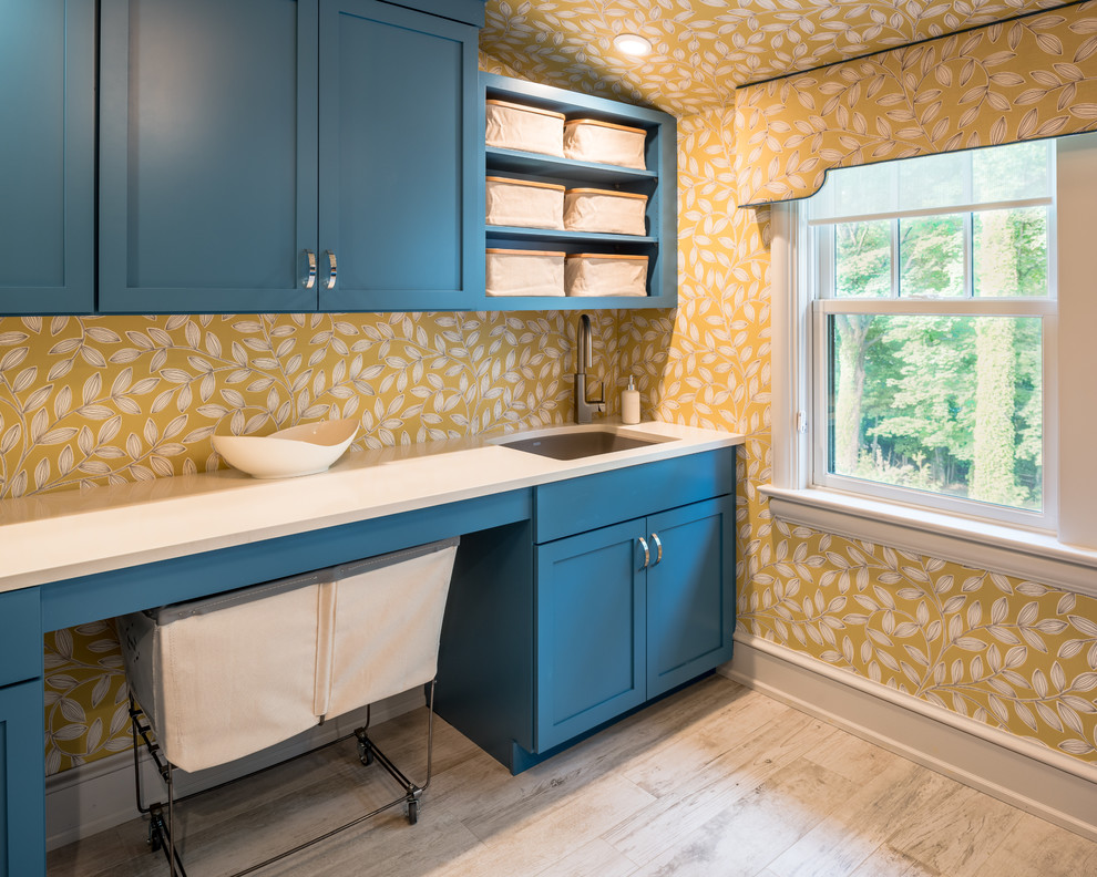 Imagen de cuarto de lavado lineal tradicional renovado con fregadero bajoencimera, armarios estilo shaker, puertas de armario azules, paredes amarillas y suelo de madera clara