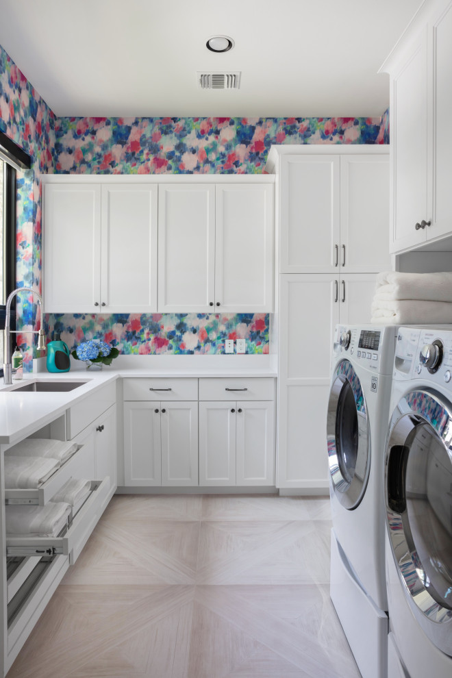 Klassisk inredning av en vita u-formad vitt tvättstuga enbart för tvätt, med en undermonterad diskho, skåp i shakerstil, vita skåp, flerfärgade väggar, en tvättmaskin och torktumlare bredvid varandra och grått golv