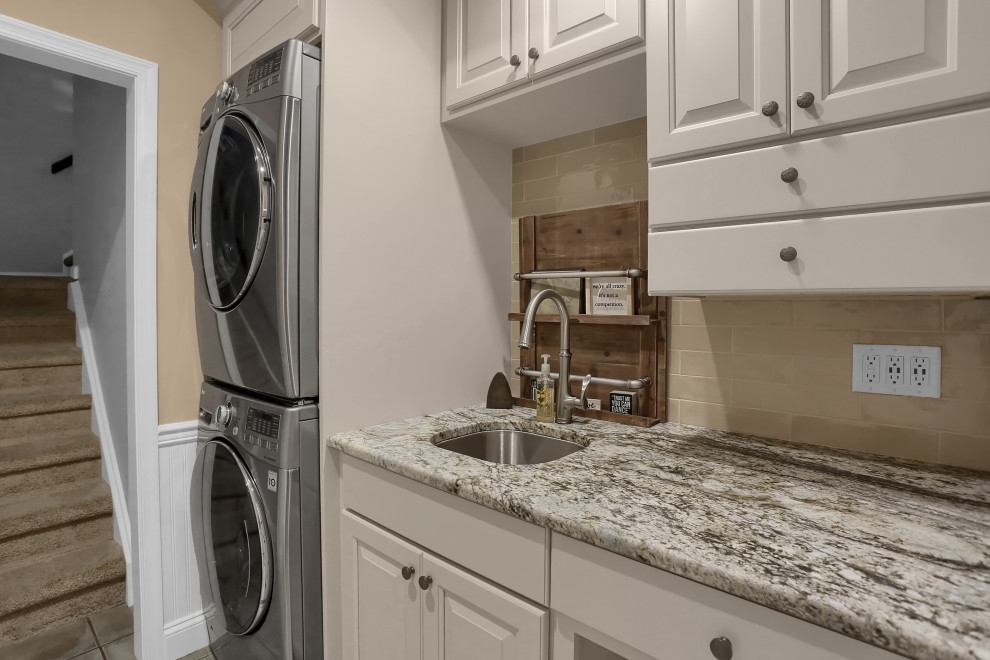 Inspiration for a mid-sized timeless single-wall dedicated laundry room remodel in Other with an undermount sink, raised-panel cabinets, white cabinets, granite countertops, beige walls, a stacked washer/dryer and white countertops