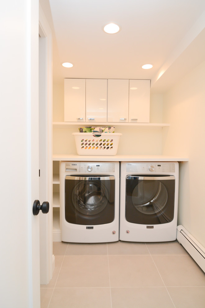 Inspiration för mellanstora moderna linjära vitt tvättstugor enbart för tvätt, med släta luckor, vita skåp, träbänkskiva, klinkergolv i porslin, en tvättmaskin och torktumlare bredvid varandra, vita väggar och grått golv