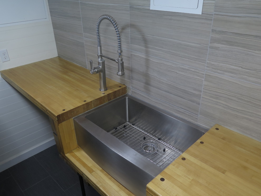 Photo of a small industrial galley separated utility room in New York with a belfast sink, wood worktops, white walls, porcelain flooring and a side by side washer and dryer.