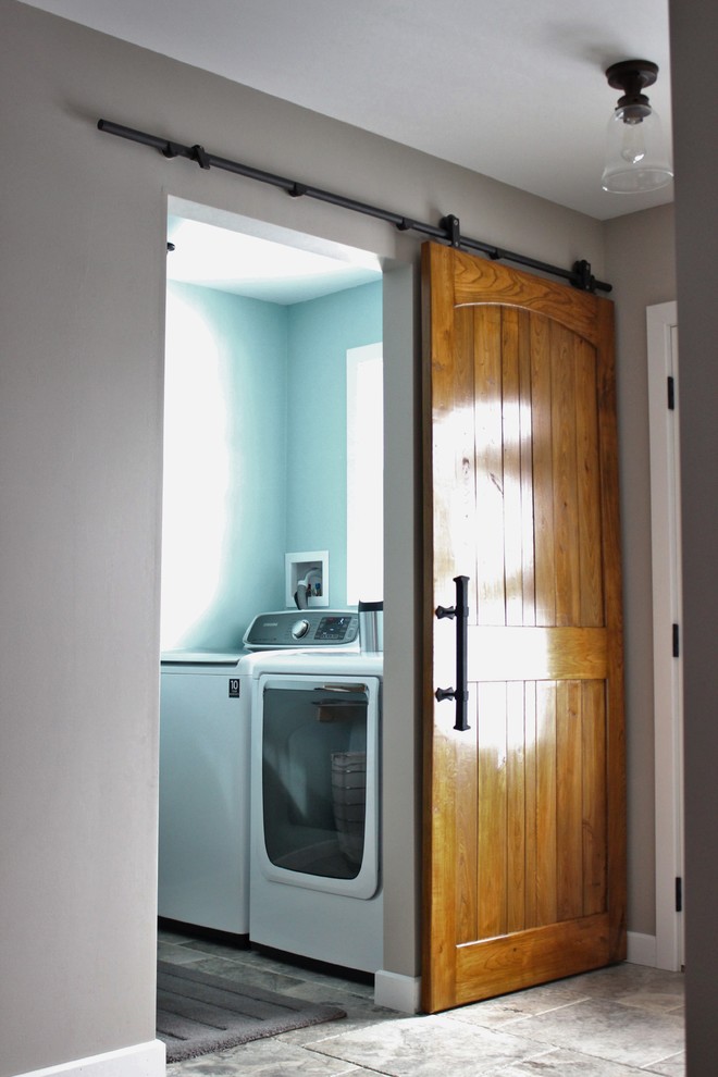 Foto på en liten industriell tvättstuga enbart för tvätt, med laminatbänkskiva, blå väggar, travertin golv, en tvättmaskin och torktumlare bredvid varandra, skåp i shakerstil och vita skåp