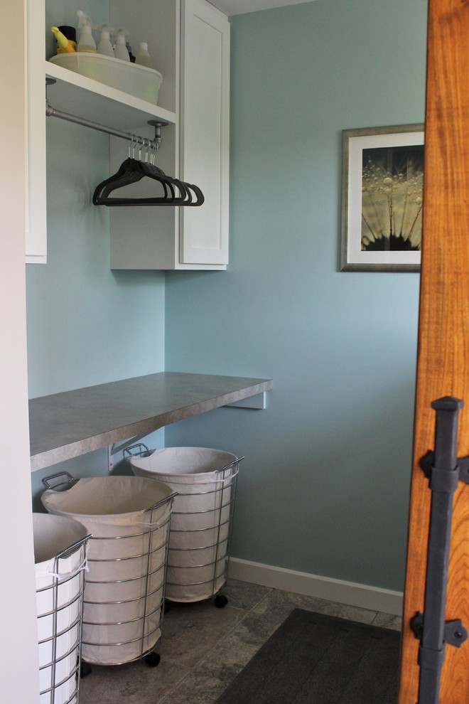 Immagine di una sala lavanderia tradizionale con ante in stile shaker, ante bianche, top in laminato, pareti blu, pavimento in travertino e lavatrice e asciugatrice affiancate
