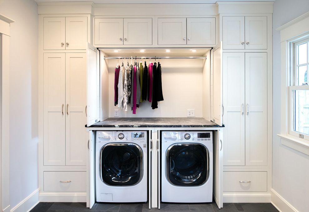 Exempel på en stor klassisk grå linjär grått tvättstuga, med skåp i shakerstil, vita skåp, bänkskiva i täljsten, skiffergolv, tvättmaskin och torktumlare byggt in i ett skåp och grå väggar
