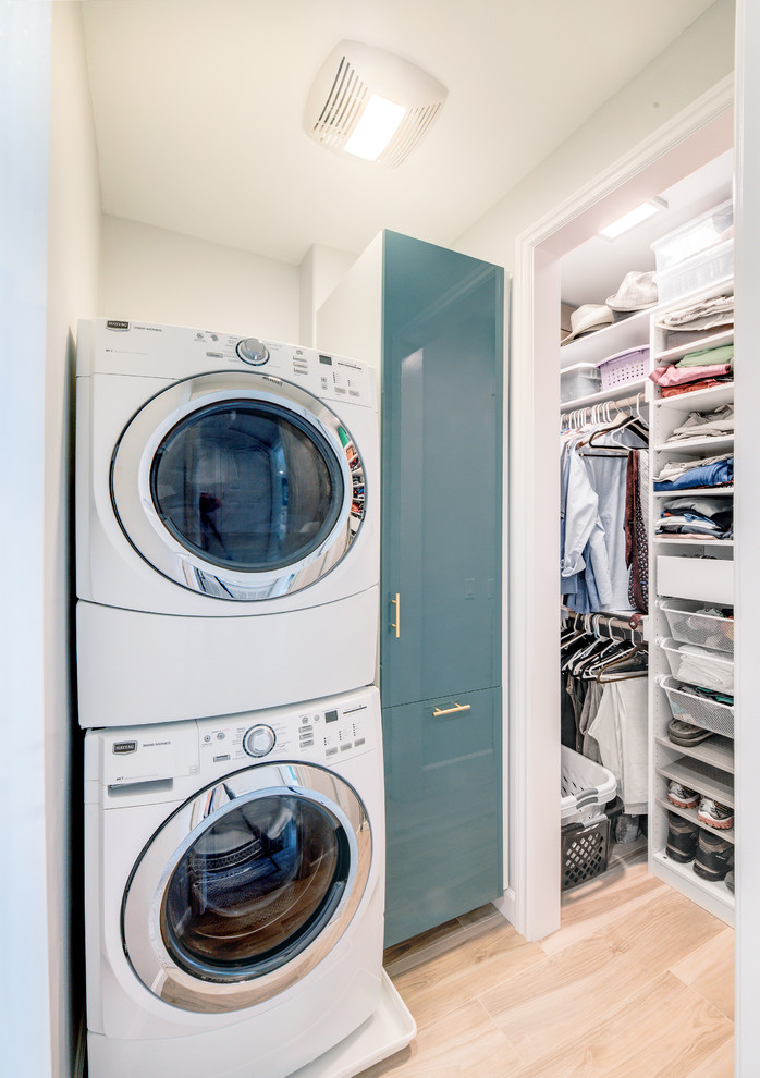 Imagen de lavadero multiusos y en L contemporáneo pequeño con armarios con paneles lisos, puertas de armario azules, paredes blancas, suelo de madera clara y lavadora y secadora apiladas