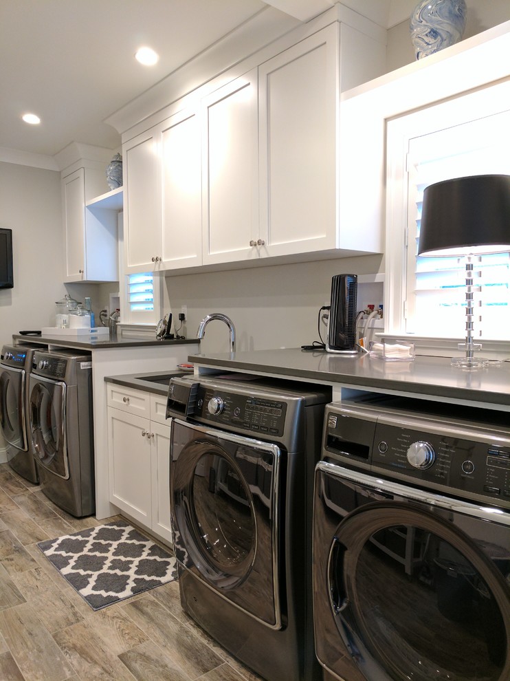 This is an example of a large traditional galley separated utility room in Philadelphia with a submerged sink, recessed-panel cabinets, white cabinets, composite countertops, grey walls, a side by side washer and dryer, grey floors and light hardwood flooring.