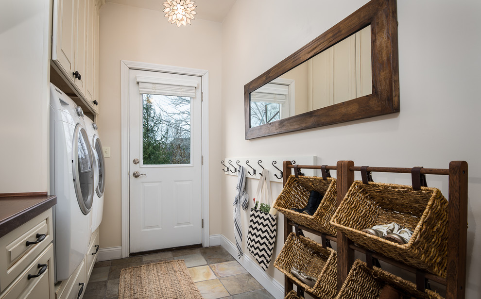 Modelo de lavadero de estilo de casa de campo con puertas de armario beige, encimera de madera y armarios con paneles con relieve