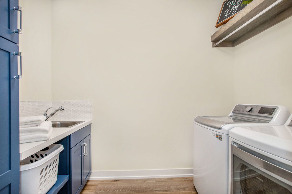 Idéer för en klassisk vita parallell tvättstuga enbart för tvätt, med en nedsänkt diskho, skåp i shakerstil, blå skåp, laminatbänkskiva, vita väggar, vinylgolv, en tvättmaskin och torktumlare bredvid varandra och brunt golv