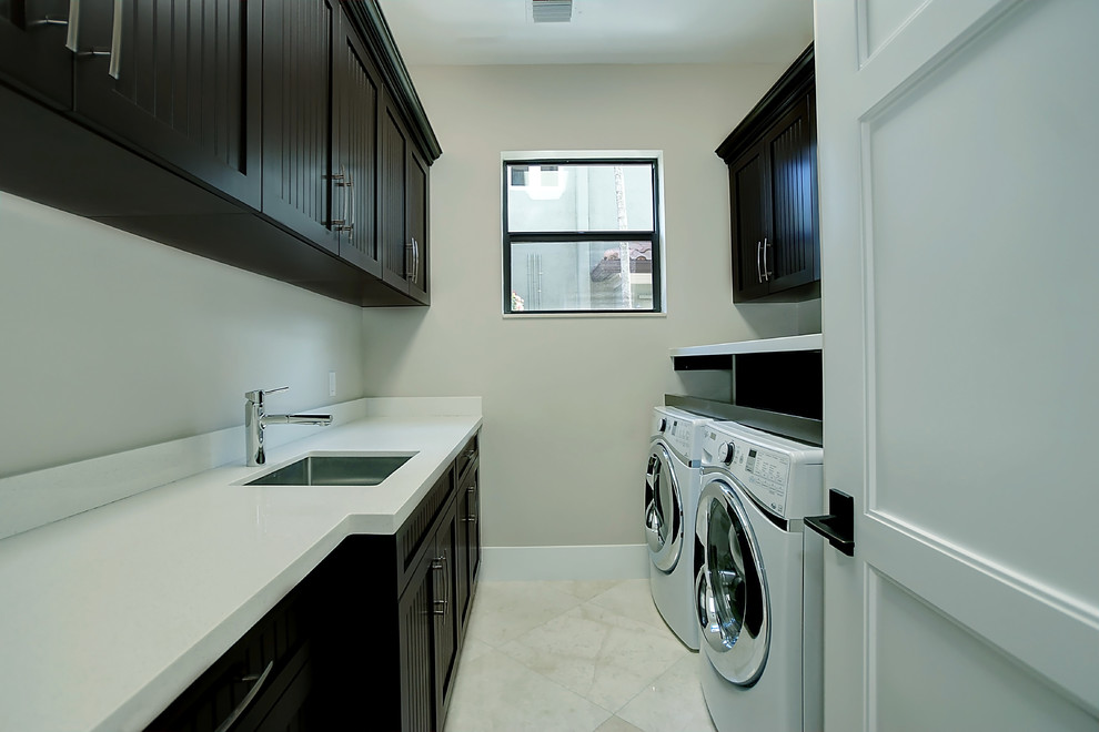 Idéer för mellanstora medelhavsstil parallella tvättstugor enbart för tvätt, med en undermonterad diskho, luckor med infälld panel, svarta skåp, bänkskiva i kvarts, beige väggar, marmorgolv, en tvättmaskin och torktumlare bredvid varandra och beiget golv