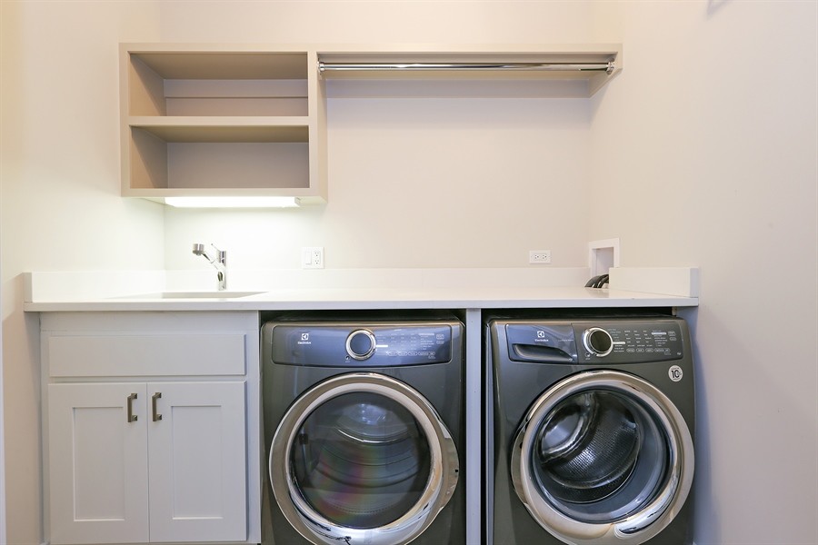 Inredning av en modern liten linjär tvättstuga, med en undermonterad diskho, skåp i shakerstil, grå skåp, bänkskiva i kvarts, grå väggar, ljust trägolv och en tvättmaskin och torktumlare bredvid varandra