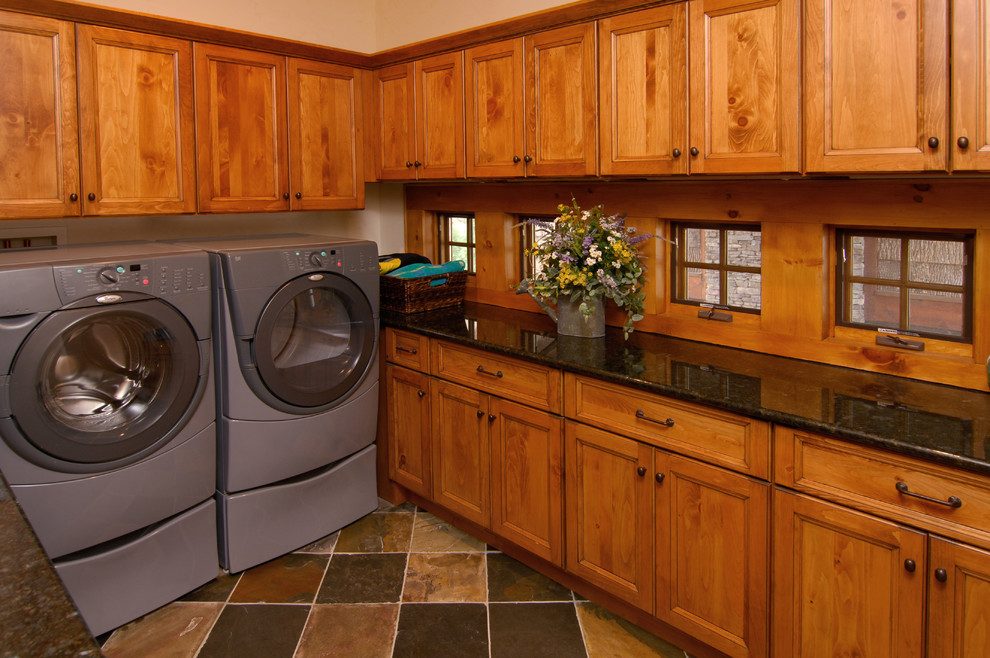 Esempio di una sala lavanderia rustica con ante con riquadro incassato, ante in legno scuro, top in granito, pavimento in ardesia e lavatrice e asciugatrice affiancate