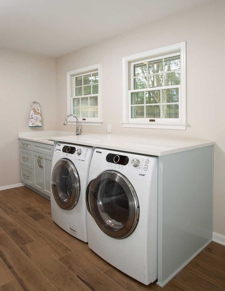 Design ideas for a medium sized traditional utility room in DC Metro with a submerged sink, recessed-panel cabinets, blue cabinets, quartz worktops, medium hardwood flooring, brown floors, white worktops, beige walls and a side by side washer and dryer.