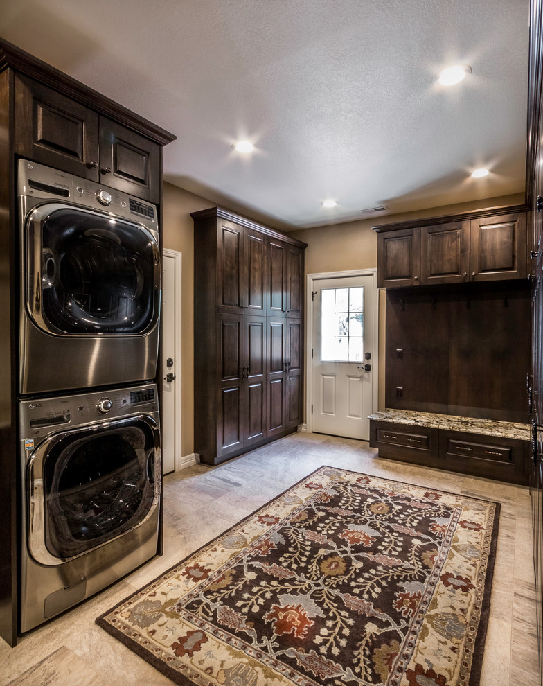 Large elegant porcelain tile utility room photo in Denver with an undermount sink, dark wood cabinets, granite countertops and a stacked washer/dryer