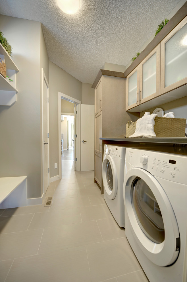 Inspiration för mellanstora moderna linjära tvättstugor enbart för tvätt, med luckor med glaspanel, skåp i ljust trä, grå väggar och en tvättmaskin och torktumlare bredvid varandra
