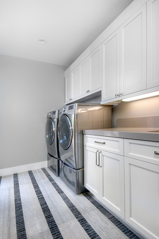 Klassisk inredning av en mellanstor linjär tvättstuga enbart för tvätt, med en undermonterad diskho, skåp i shakerstil, vita skåp, bänkskiva i kvarts, grå väggar, klinkergolv i porslin, en tvättmaskin och torktumlare bredvid varandra och flerfärgat golv