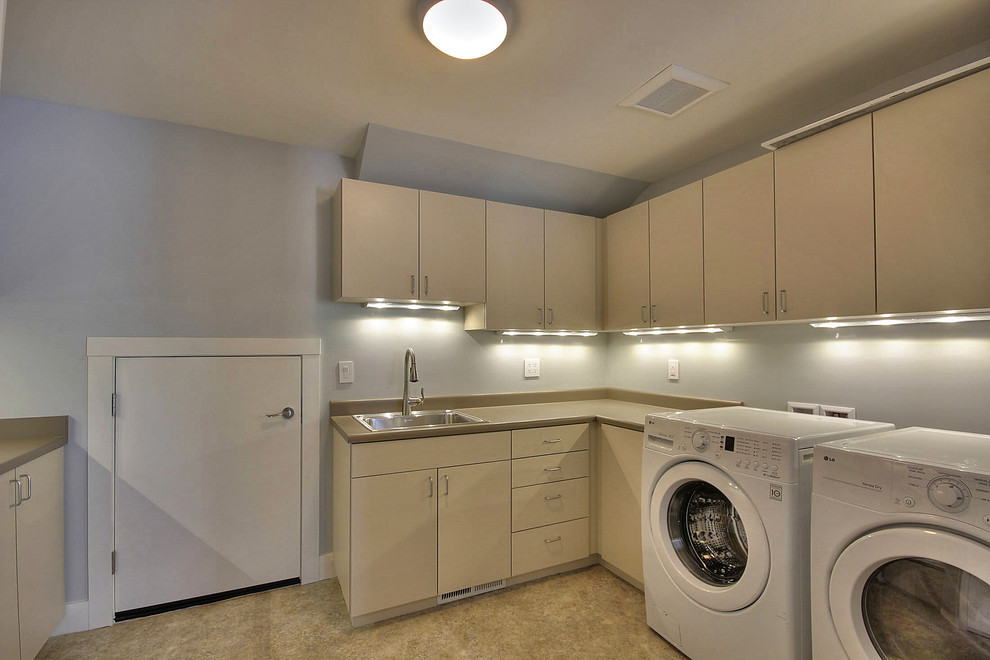 Exempel på en stor l-formad tvättstuga enbart för tvätt, med en enkel diskho, släta luckor, beige skåp, grå väggar och en tvättmaskin och torktumlare bredvid varandra