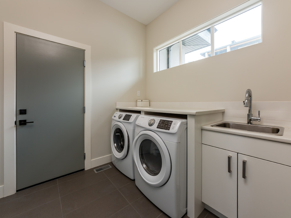 Inspiration for a mid-sized coastal galley ceramic tile and gray floor dedicated laundry room remodel in Other with an utility sink, flat-panel cabinets, white cabinets, laminate countertops, beige walls, a side-by-side washer/dryer and beige countertops