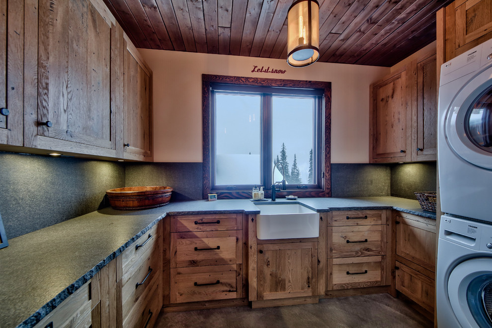 Photo of a large rustic l-shaped separated utility room in Vancouver with a belfast sink, flat-panel cabinets, concrete worktops, beige walls, concrete flooring, a stacked washer and dryer and medium wood cabinets.