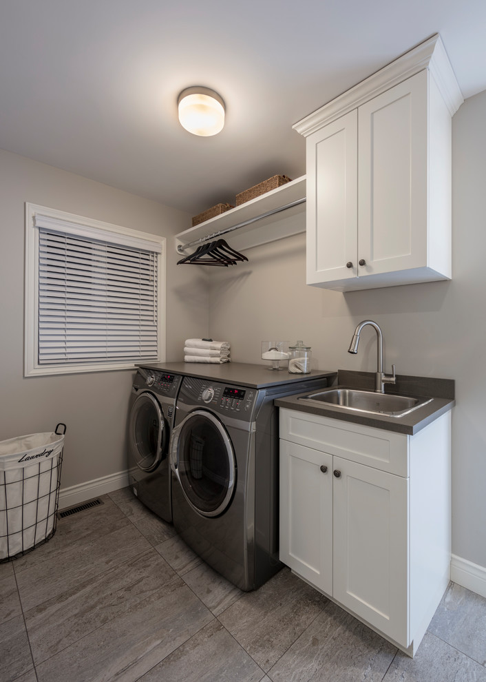 Exempel på en klassisk grå grått tvättstuga, med en nedsänkt diskho, skåp i shakerstil, vita skåp, bänkskiva i kvarts, grå väggar, en tvättmaskin och torktumlare bredvid varandra och grått golv
