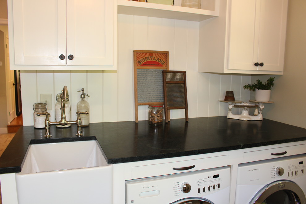 Foto på en liten lantlig tvättstuga, med en rustik diskho, luckor med infälld panel, vita skåp, bänkskiva i täljsten, gröna väggar, travertin golv, en tvättmaskin och torktumlare bredvid varandra och beiget golv