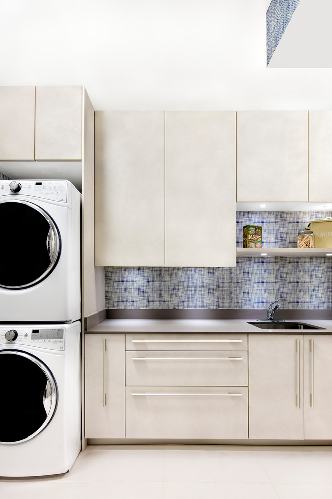 Exempel på en klassisk linjär tvättstuga, med en undermonterad diskho, släta luckor, grå skåp, bänkskiva i kvarts, blå väggar, en tvättpelare och vitt golv