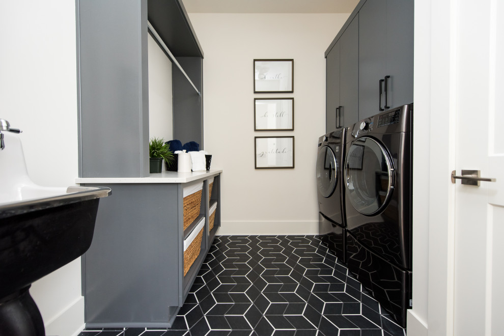 Esempio di una sala lavanderia moderna di medie dimensioni con lavello da incasso, ante lisce, ante blu, top in quarzo composito, lavatrice e asciugatrice affiancate, pavimento nero e top bianco