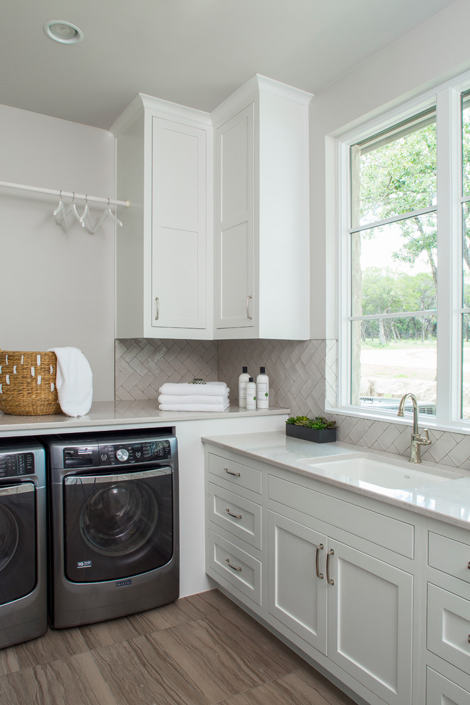 Klassischer Hauswirtschaftsraum in L-Form mit Unterbauwaschbecken, Schrankfronten im Shaker-Stil, weißen Schränken, weißer Wandfarbe, braunem Holzboden und Waschmaschine und Trockner nebeneinander in Austin
